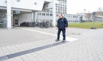 Ein Mann läuft mit seinem Stock auf dem Weg zur Freiburger Augenklinik und testet damit das neue Leitsystem für sehbehinderte Menschen